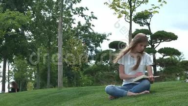 公园里年轻漂亮的女孩正在看书。一个学生正在翻阅一本书。坐在草地上